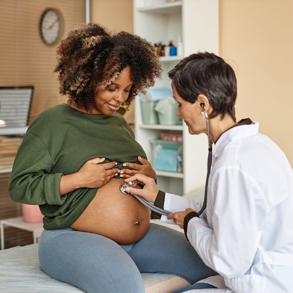 Doctor listening to pregnant mother's stomach using stethoscope