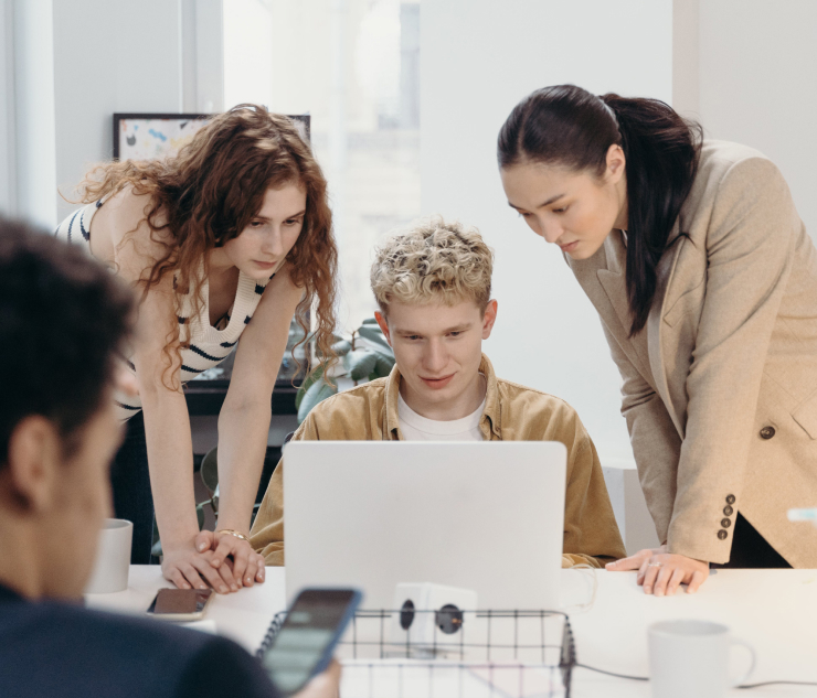 Four individuals around laptop in office, three standing one seated
