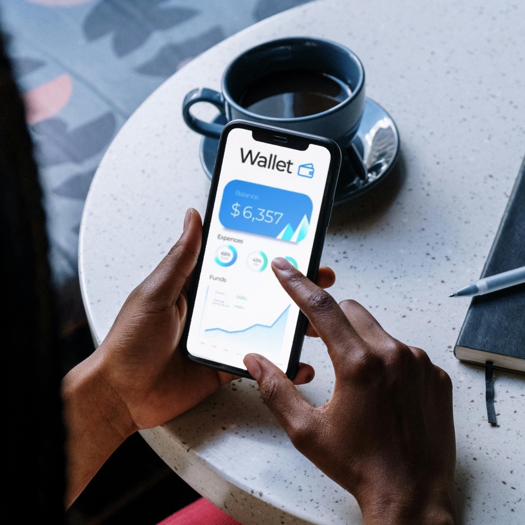 Person holding smartphone with finance app, balance shown, coffee nearby