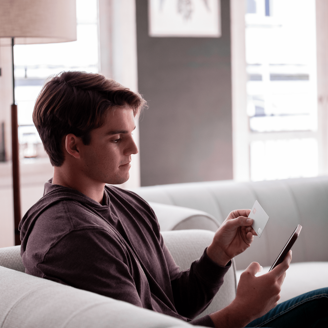Individual on couch holding a credit card and mobile phone